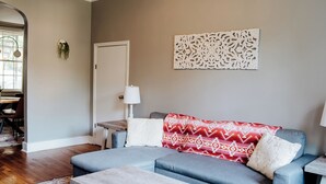 Een woonkamer met een grijze bank, een witte salontafel, een kamerkleed met dessin en een plafondlamp.
