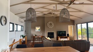 A modern living room with a large sectional sofa, a dining table, and a TV. There are two hanging light fixtures and a ceiling fan.