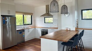 A modern kitchen with white cabinets, stainless steel appliances, a wooden island with bar stools, and pendant lighting.