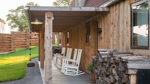 A wooden cabin with a covered porch, rocking chairs, and a stack of firewood. - Unique 3 bedroom barn with a fireplace and pond (Sarver)