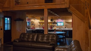 A spacious living area with a leather sofa, a dining table, and a kitchen in the background. - Unique 3 bedroom barn with a fireplace and pond (Sarver)
