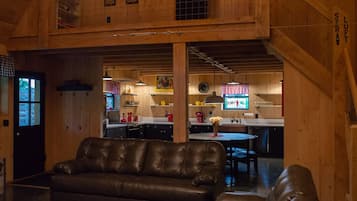 A spacious living area with a leather sofa, a dining table, and a kitchen in the background.