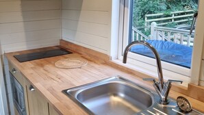 A modern kitchen with a wooden countertop, stainless steel sink, and a window with a view of a wooden deck and greenery. - Glamping Hut - Sleeps 2, hot tub & parking (Welshpool)