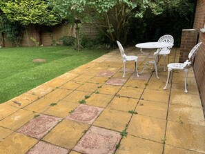 A patio with a table and chairs, a brick wall, and a grassy area.