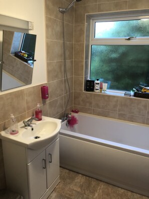 Bathroom features a bathtub, sink, and showerhead, with a window offering a view of the outdoors.