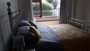 A bedroom with a bed, pillows, a lamp, and a window with curtains. - Lovely 1-Bed Apartment at Whitepark Bay Co Antrim (Bushmills)