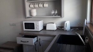 A kitchen with a microwave, toaster, kettle, and a shelf with cups and bowls. - Lovely 1-Bed Apartment at Whitepark Bay Co Antrim (Bushmills)
