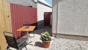A patio with a wooden table and chairs, a red fence, and a potted plant. - Lovely 1-Bed Apartment at Whitepark Bay Co Antrim (Bushmills)