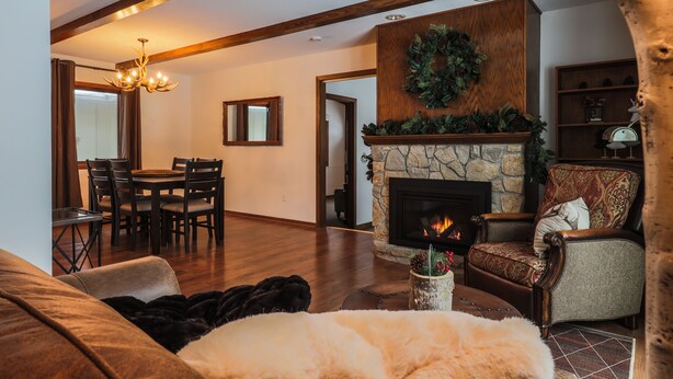 A cozy living room with a fireplace, wooden beams, a dining area, and a fireplace mantle with greenery.