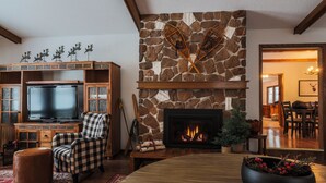 A cozy living room with a stone fireplace, a television, and a checkered armchair.