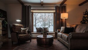 A cozy living room with a fireplace, a large window, and a Christmas tree.