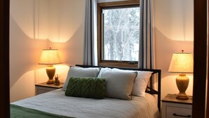 A neatly made bed with a green pillow, two bedside lamps, and a window with curtains.