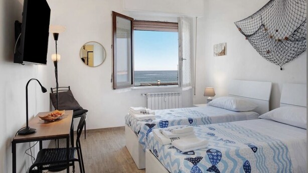 Een hotelkamer met een bed, een bureau met stoel, een raam met uitzicht op zee en een aan de muur bevestigde televisie.