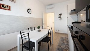 Een compacte keuken met een wit aanrecht, een fornuis, en een eethoek met een witte tafel en zwarte stoelen.