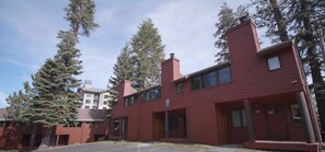 Un bâtiment rouge avec une cheminée, deux places de stationnement et de grands arbres en arrière-plan.