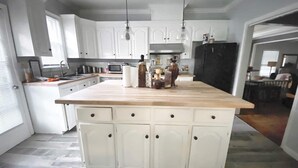 Een keuken met witte kasten, een houten aanrecht en een centraal eiland met lades.