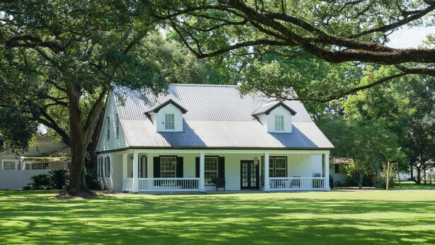 Een tweelaags huis met een veranda, omgeven door een verzorgd gazon.