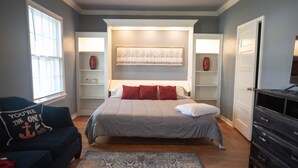 Een slaapkamer met een bed, een stoel, een dressoir en een raam.