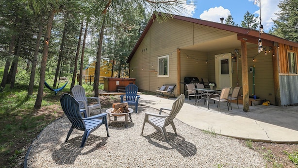 Una cabaña con mobiliario exterior, una fogata y un patio cubierto.