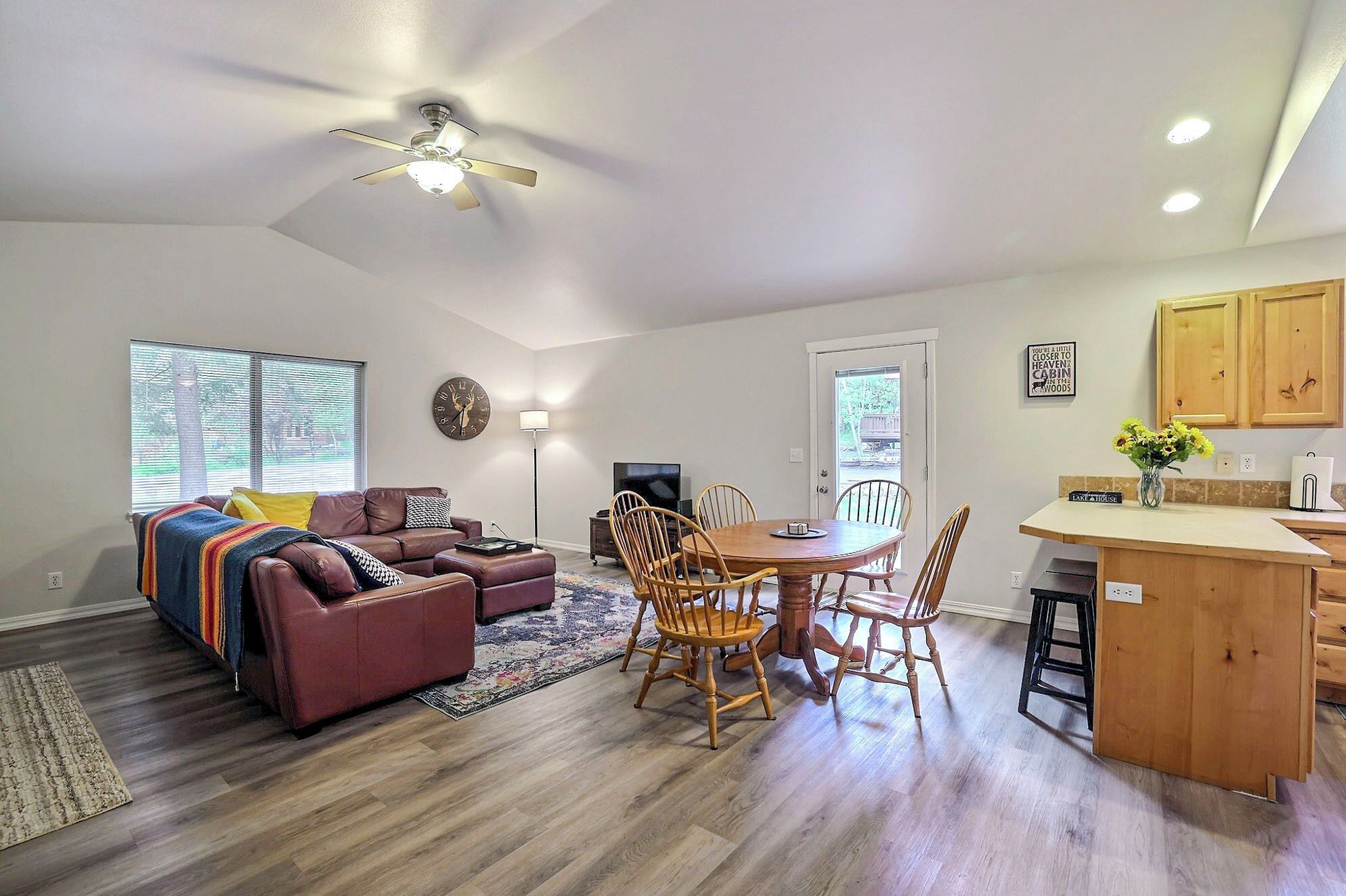 A modern living room with a sofa, chairs, a dining table, and a kitchen area with wooden cabinets.