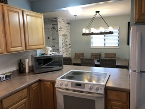 A kitchen with wooden cabinets, a microwave, a stove, wicker chairs, and a ceiling light fixture.