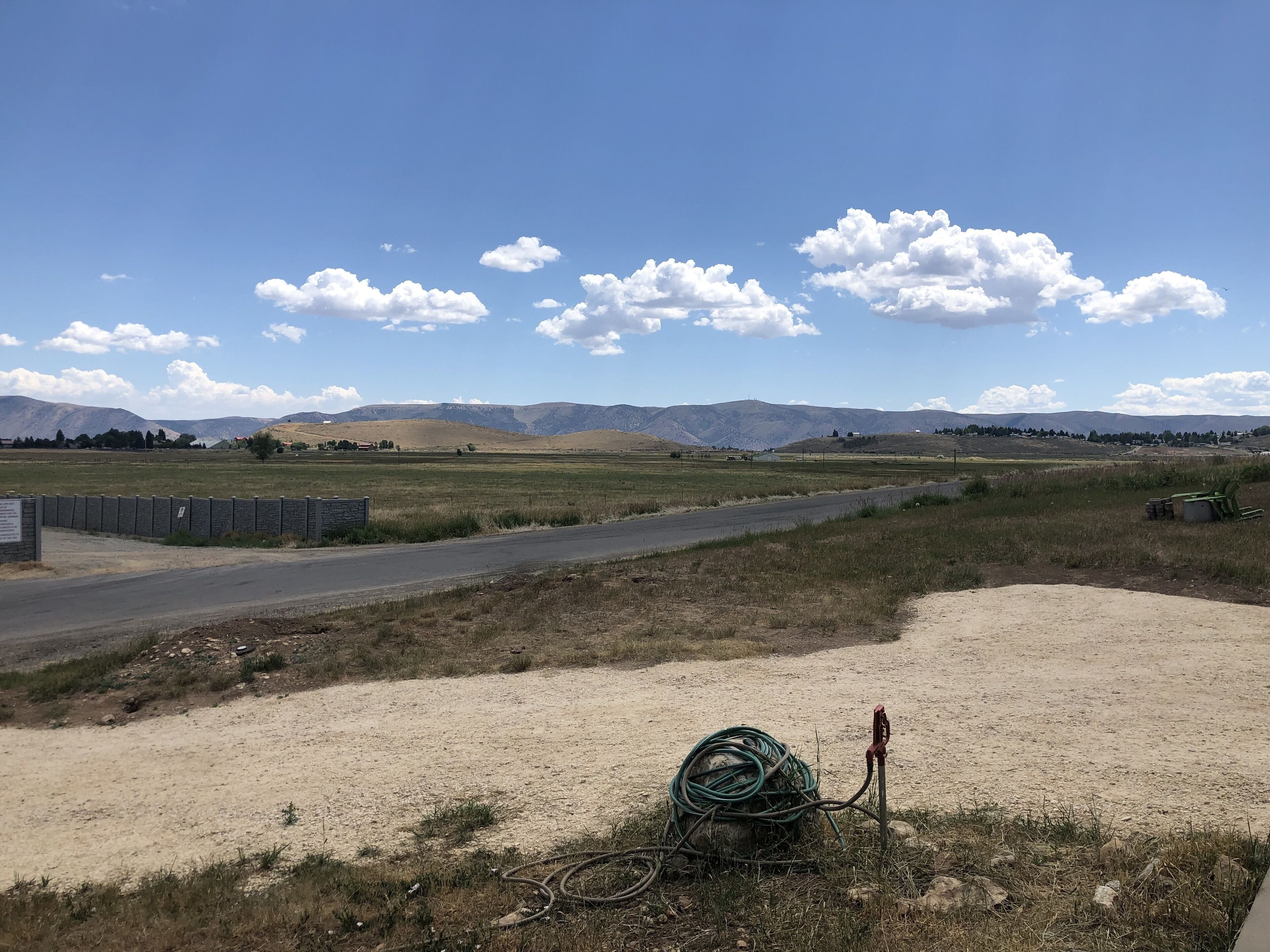 A rural landscape with a dirt road, a stone wall, and mountains in the background.