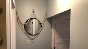 Een gang met een ronde spiegel, omlijst door een geweven ontwerp, een deur met horizontale panelen en een lichtschakelaar aan de muur.