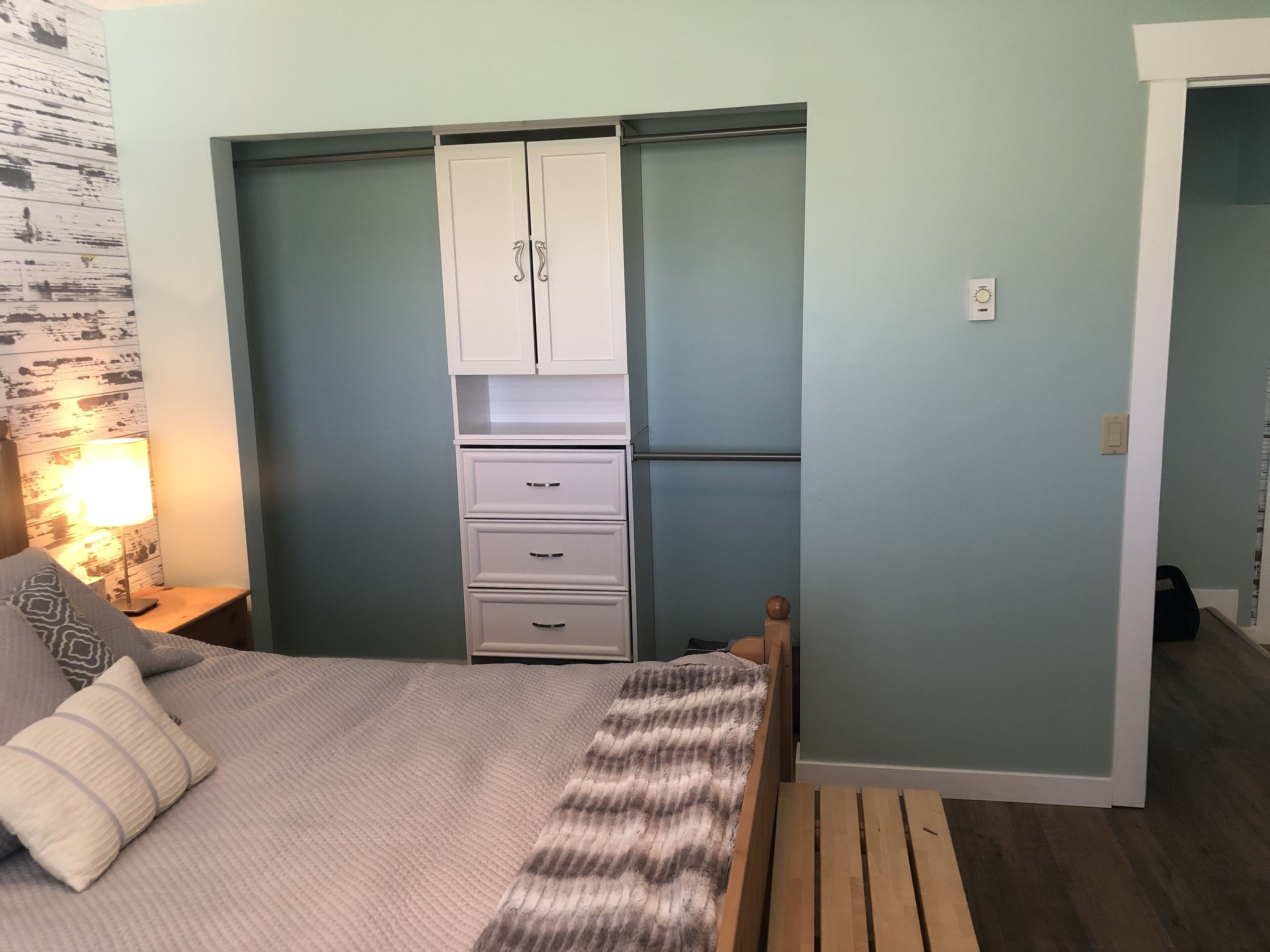 Une chambre à coucher comprenant un lit, une armoire, une table de chevet avec une lampe et un banc en bois.