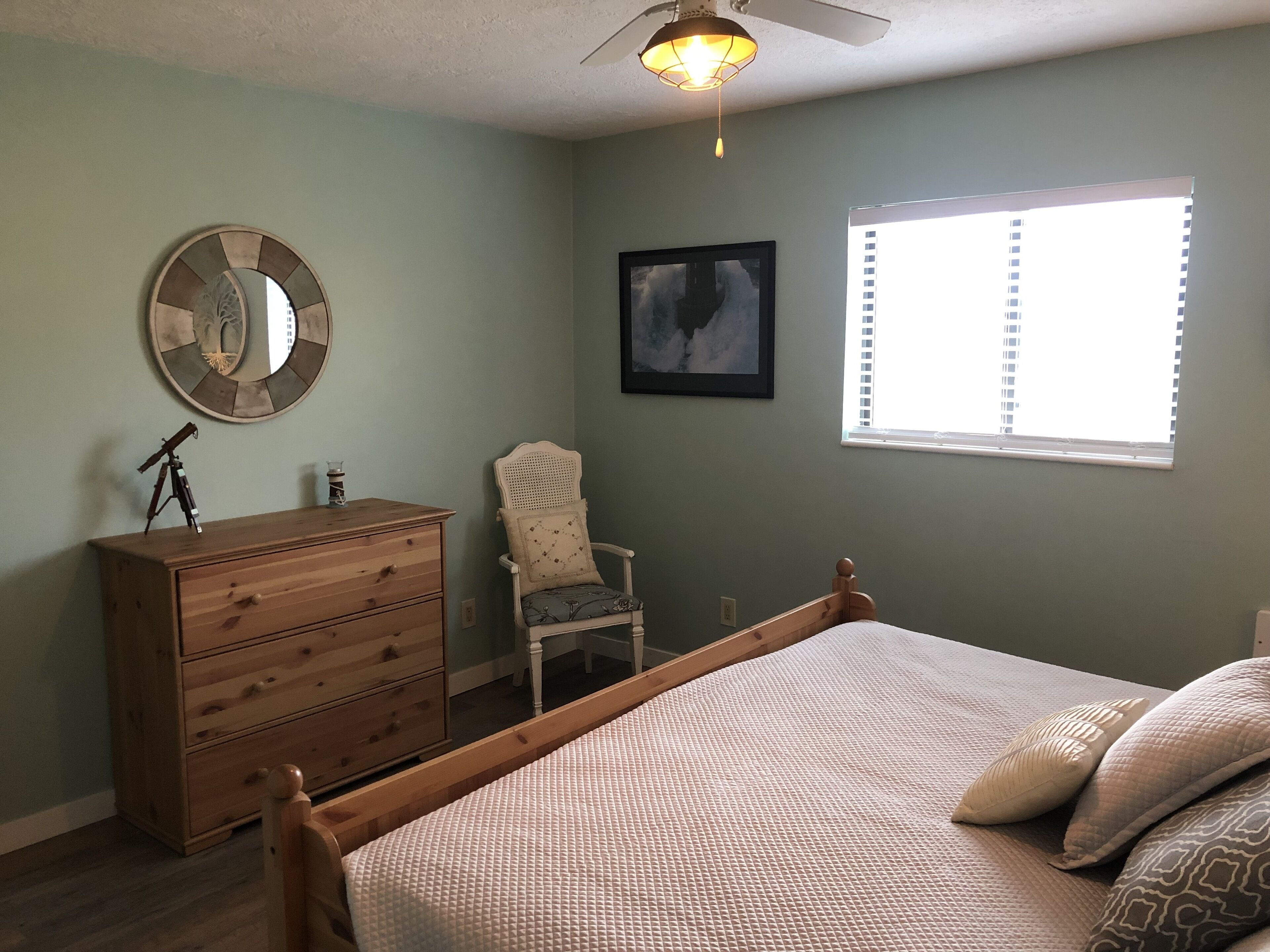 A bedroom with a bed, dresser, chair, and a wall-mounted mirror.