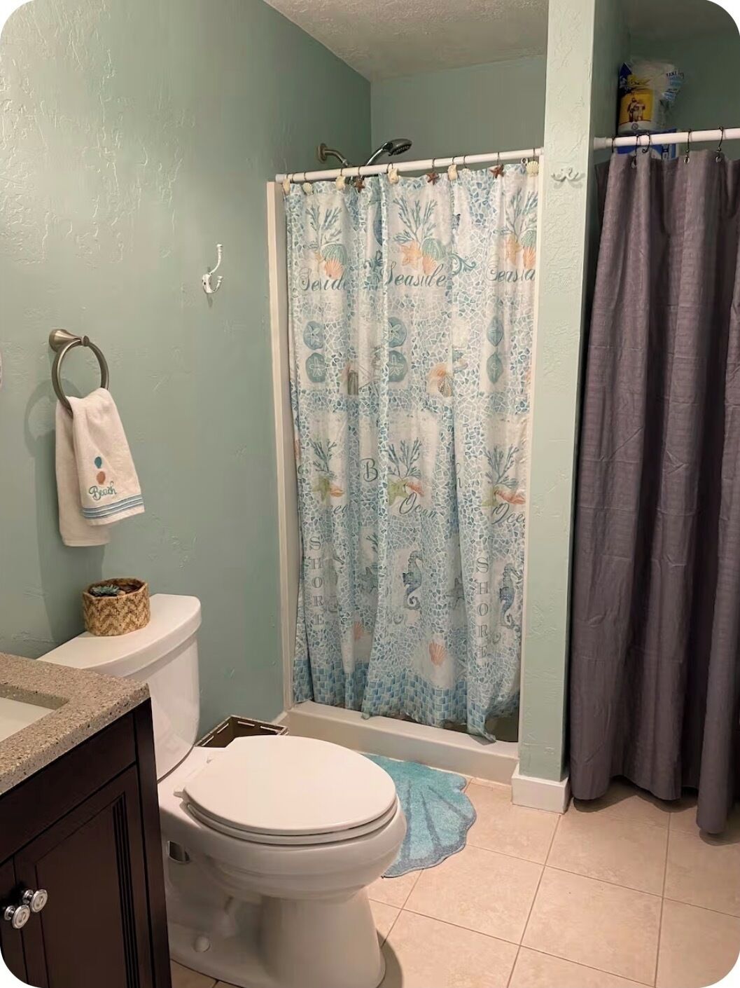 Une salle de bain avec des toilettes, un rideau de douche orné d’un motif sur le thème de la mer, et une serviette accrochée au mur.