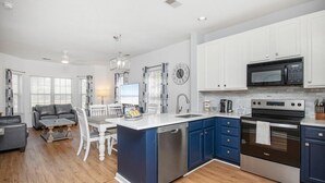 A modern kitchen with white and blue cabinetry, stainless steel appliances, and a central island. - Legends Golf Resort Condo, 4 Beds, 2 Bath Pool access near Coastal Carolina Univ (Myrtle Beach)