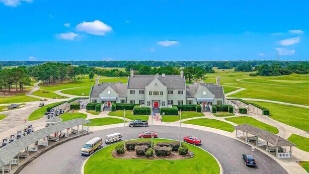 A large, two-story building with a symmetrical facade, a central entrance with a flag, and a well-maintained lawn in front. - Legends Golf Resort Condo, 4 Beds, 2 Bath Pool access near Coastal Carolina Univ (Myrtle Beach)