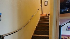 Un escalier recouvert de moquette, muni d’une chaîne servant de barrière, de rampes en bois et d’un tableau encadré accroché au mur.