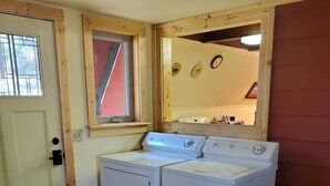 Une buanderie équipée d’un lave-linge et d’un sèche-linge, avec une petite fenêtre, un miroir et une poubelle.