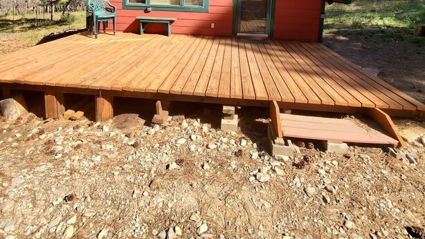 Une cabane rouge avec une terrasse en bois, deux fenêtres et une porte.