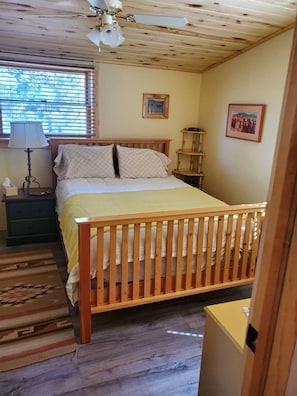 Une chambre à coucher avec un lit en bois, une table de chevet, une lampe, une fenêtre avec des stores et une horloge murale.