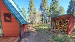 Une cabane rouge avec un toit en métal, une terrasse en bois et une pile de bois de chauffage.