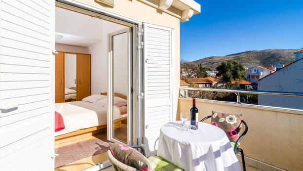 A balcony with a table, chairs, and a bed with a view of a hillside. - Relaxing Duplex Apartment A3, Close to the Sunset Beach Near Dubrovnik, 2-4 (Dubrovnik)