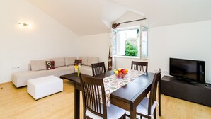 A modern living room with a dining area, a sofa, a television, and a window with a view of greenery. - Relaxing Duplex Apartment A3, Close to the Sunset Beach Near Dubrovnik, 2-4 (Dubrovnik)