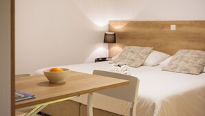 Habitación de hotel ordenada con cama, mesita de noche con frutero, lámpara y una silla.