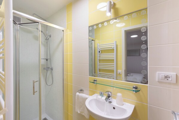 Une salle de bain dotée d’une douche à parois de verre, d’un lavabo blanc avec une étagère en verre et d’un miroir orné d’un cadre décoratif.