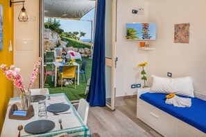 Ein Zimmer mit einem Bett, einem Esstisch mit Stühlen, einem Fernseher und Blick ins Freie.