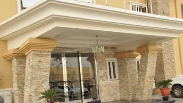 A hotel entrance with a glass door, stone pillars, and a potted plant. - Room-nippon Grand Hotels - Apartment And (Abuja)