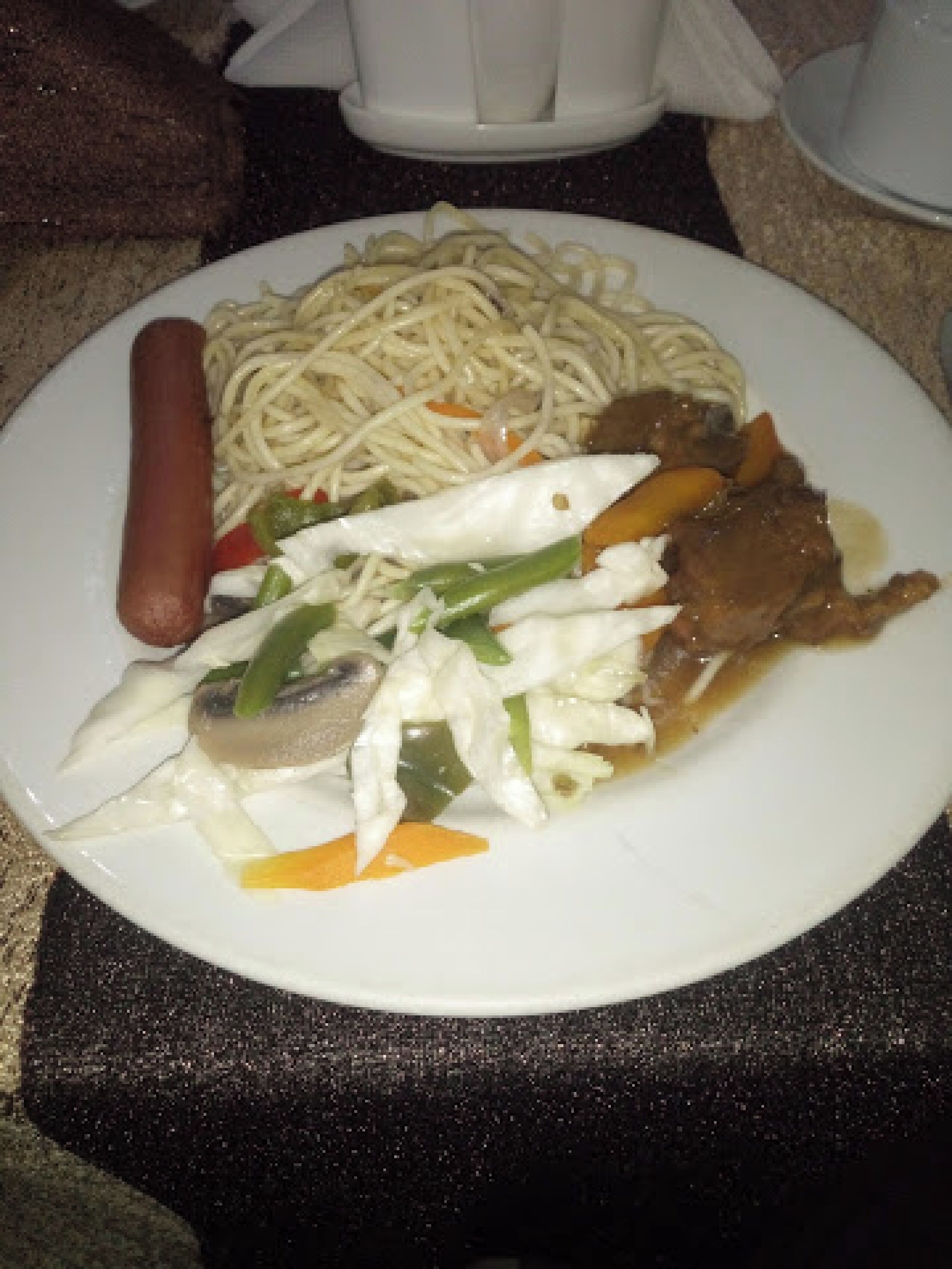 Une assiette contenant des nouilles, une saucisse, des légumes et un morceau de viande.