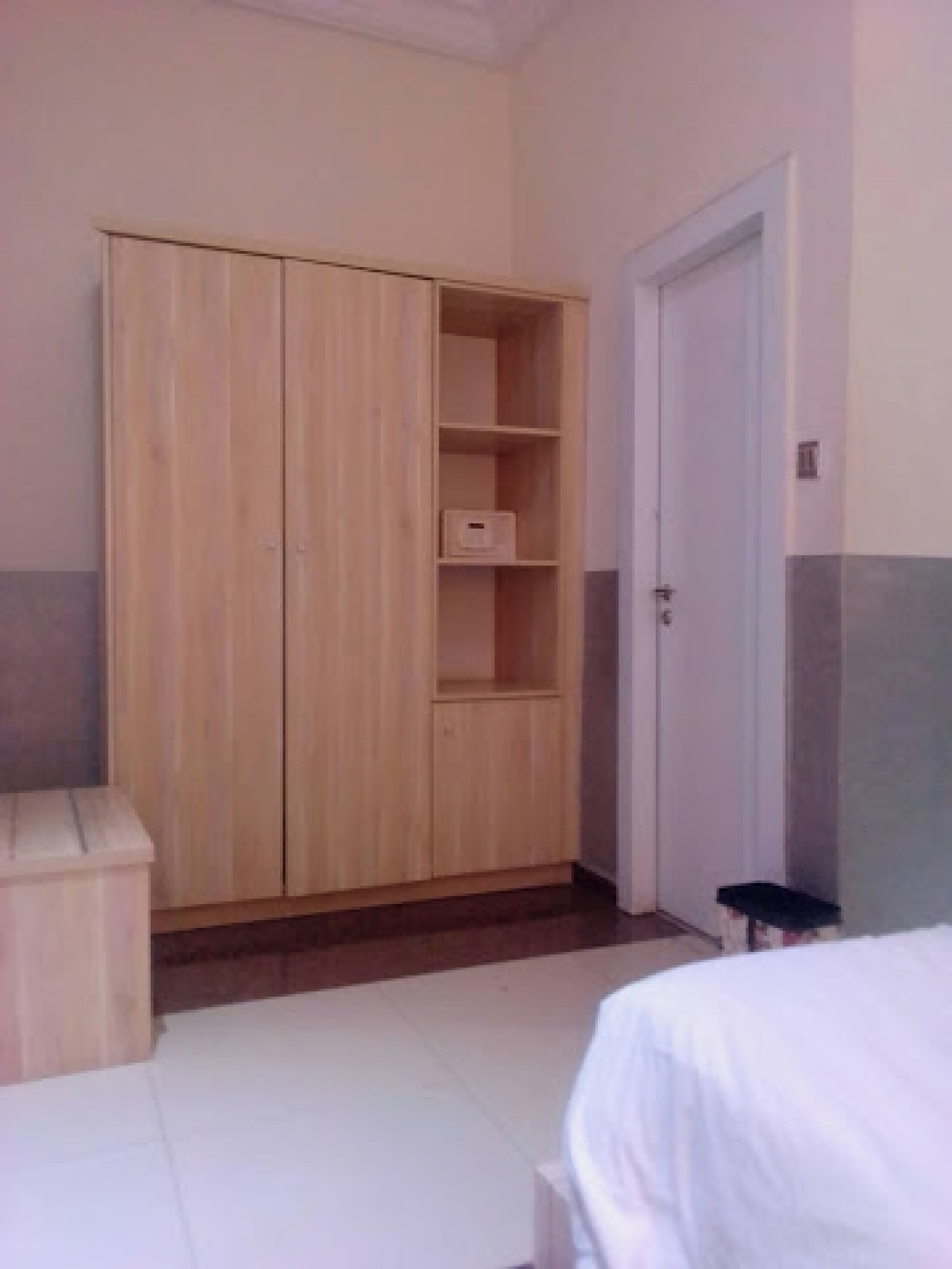 A room with a wooden wardrobe, a white bed, and a door.