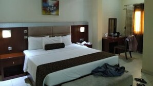 A hotel room with a bed, a desk, a chair, and a painting on the wall. - Room-nippon Grand Hotels - Apartment And (Abuja)