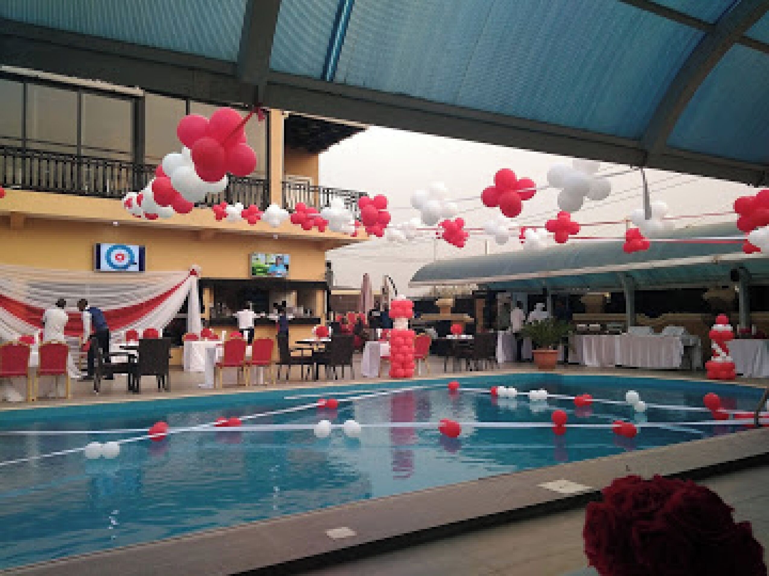 An indoor swimming pool with red and white decorations, tables, and chairs arranged for an event.