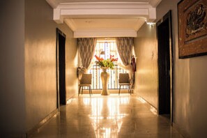A hallway with a polished floor, a vase with flowers, and two chairs. - Room-oragon Hotel - Guest Room (Lagos)