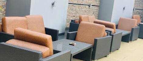Outdoor seating with cushioned chairs and tables, a brick wall, and a metal door.