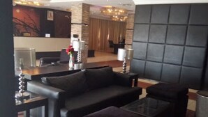 Un salon moderne comprenant un canapé, un pouf et une table basse, un coin repas avec des chaises, et un grand mur rembourré.